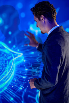 Businessman in dark suit and tie standing before a glowing security shield with a tablet outlines the roadmap with open hands during a product launch rehearsal in a dark high tech auditorium