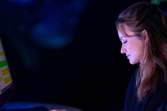 Two diverse businesswomen working late at trading desks with warm screen light on their faces murmur about the market move during a product launch rehearsal in a dark high tech auditorium