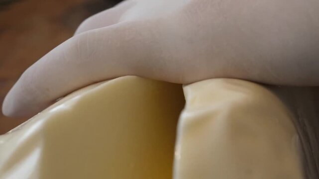 Close-up shot of an unrecognizable chef or baker using a sharp metal knife to slice a soft, glossy log of fresh mozzarella or provolone cheese on a wooden table. Professional food preparation process 