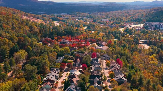 Scenic mountain community with private homes surrounded by dense woodland glowing with vibrant autumn colors. Aerial view of peaceful countryside living.