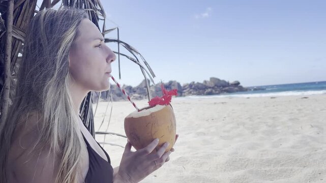 Caucasian young wife drinking a coconut in the beach. Static view