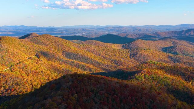 Spectacular fall landscape featuring vibrant mountain forest canopies glowing beneath colorful sunset. Brilliant autumn colors transform the surrounding countryside.
