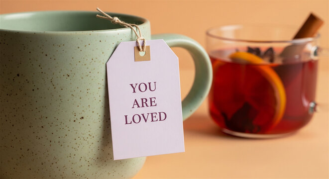 Inspirational tea tag with You Are Loved text, ceramic mug with positive message, warm winter drink with cinnamon and orange