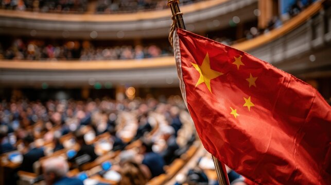 A Chinese flag is prominently displayed in a crowded conference or parliamentary hall with attendees seated in the background.
