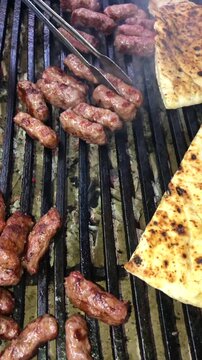 Chef flipping delicious grilled traditional kebabs and warming bread on a barbecue grill, close up
