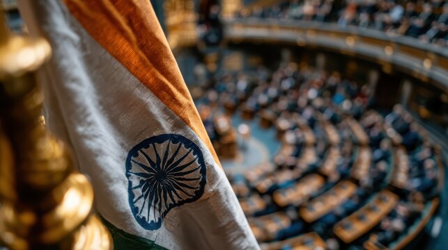 The Indian flag is prominently displayed inside a parliamentary chamber filled with seated individuals attending a session.