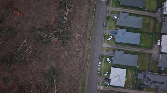 Cleared land directly adjacent to suburban homes, drone top down orbit descend along road and fenceline