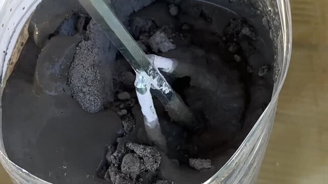 Mixing liquid cement for construction, Close-up of liquid cement being mixed in a plastic container