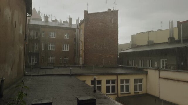 Heavy rain pours over old apartment buildings and rooftops in historic European city center in Krakow - static shot, layered composition, brick walls