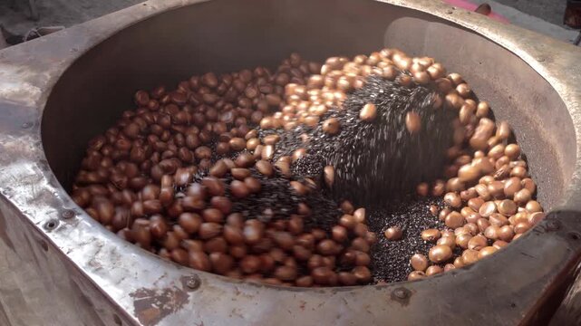 Glossy roasted chestnuts tumble through hot black roasting sand inside a rotating steel drum a traditional Chinese street food technique known as tangchaolizi (sugar-roasted chestnuts) loop-ready shot