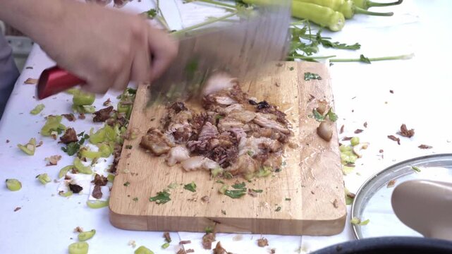 A chef finely mince braised pork shoulder with a cleaver on a wooden chopping board, preparing the filling for a Chinese-style meat sandwich (rou jia mo) Fresh cilantro, celery, and green chili pepper