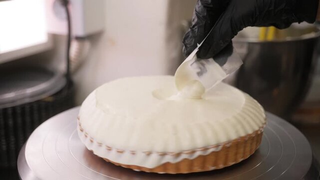 Close-up footage of a professional baker in black gloves meticulously decorating a fresh lemon meringue tart on a rotating cake stand. The chef uses a specialized leveling tool to create a beautiful, 