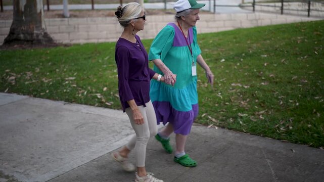 Mature daughter visits her elderly mother in a park where they walk together and share photos and stories while enjoying their time.