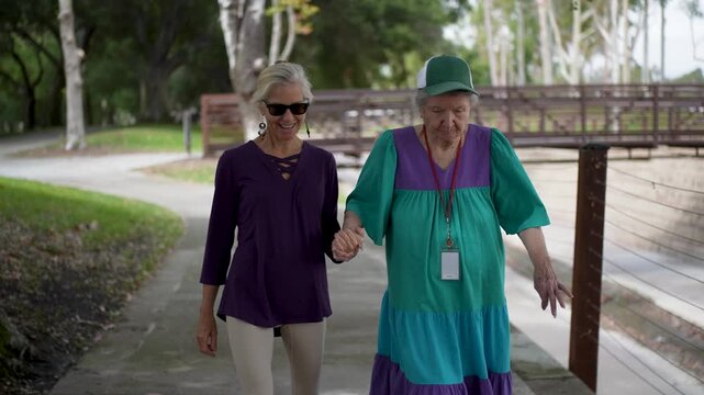 Mature daughter visits her elderly mother in a park where they walk and talk, sharing stories and enjoying their time together.