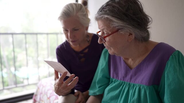 Mature daughter visits her elderly mother at a senior care facility where they share photos and talk about past times together.