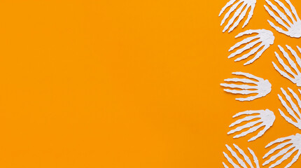 Fototapeta premium Halloween orange background featuring skeleton hand paper cut out right border, copy space for spooky party invitation, greeting card, banner, poster, flyer and creepy autumn holiday design