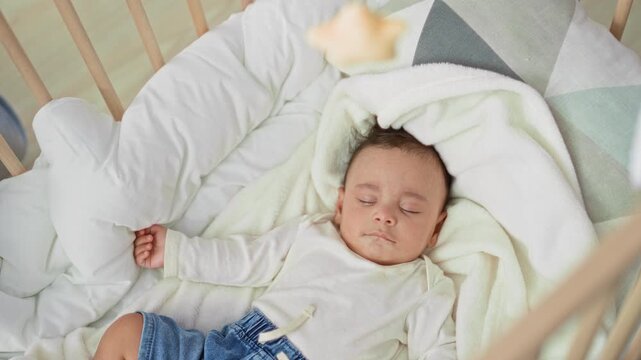 Hispanic toddler boy sleeping on his back in a wooden cradle bed with white blanket and denim shorts, hand curled on pillow in nursery; peaceful rest.