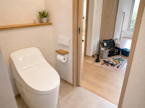 Newly renovated bathroom with toilet and construction tools in background.