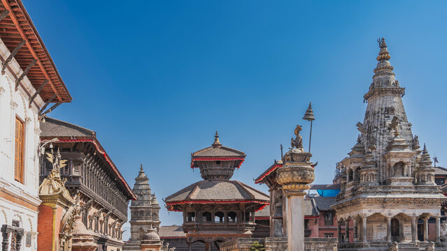 The famous ancient Newar architecture. Temples with high domes, a multi-tiered pagoda against the blue sky. A Bhupatindra Malla king  statue sitting on a tall column. Nepal. Kathmandu. Durbar Square