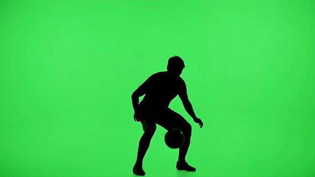 Silhouette Soccer Player Trapping Ball on Green Screen - A black silhouette of a soccer player is captured in motion, skillfully trapping a soccer ball against a vibrant green screen background.