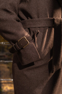 A close-up commercial shot of a stylish chocolate brown wool coat featuring a belted cuff detail in harsh daylight