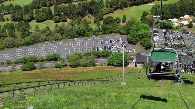 Scenic frame from funicular on Mount Omuro in Izu, Japan, with chairlift descending over green hillside, forest, sea view and sunny outdoor atmosphere. Ideal for travel, adventure and landscape themes