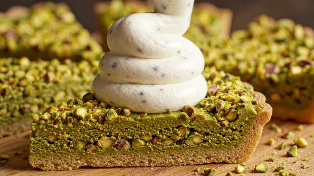 Piping whipped cream onto a pistachio tart slice in slow motion