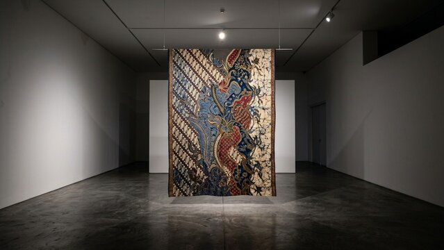 Traditional Indonesian batik cloth exhibition inside a minimalist art gallery with directional spot lighting