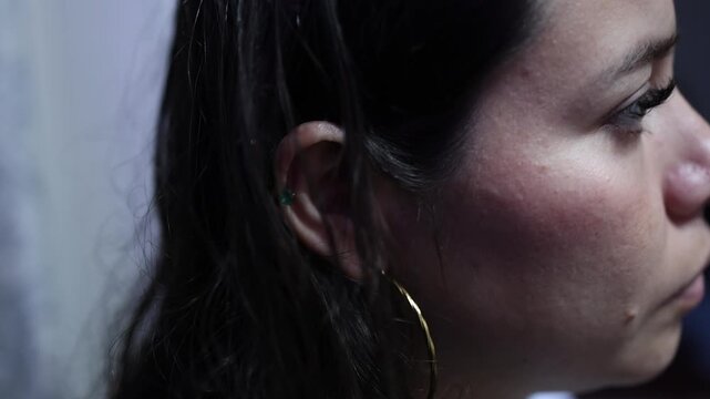 Tense close-up shot of a young woman with gold hoop earring taking a serious call on smartphone, low light ambiance highlights emotion, soft focus, shallow depth of field, cinematic feel.