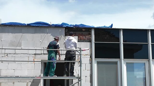 Construction workers on scaffolding installing windows on a building facade. Workers in safety gear are seen on scaffolding, actively engaged in the process of installing windows onto a building under