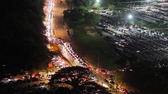 Aerial night view of congested road and packed parking lot with vehicle light trails at Batu Kawan Stadium