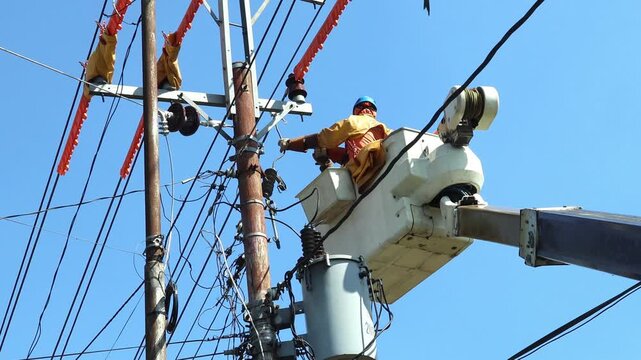 Two Utility Lineworkers in Full PPE Performing Live-Line Connection of a Single-Phase Distribution Transformer to a 20kV Overhead Power Line Using a Crane Truck