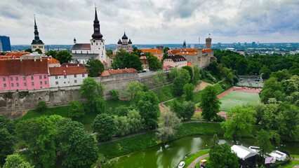 Tallinn Old Town's medieval city walls line a green park featuring Snelli pond, with historic church spires and buildings defining the urban landscape under a cloudy sky © Dark Artistic