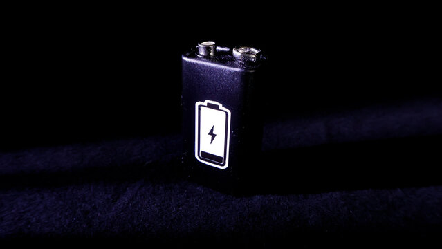 Black 9V battery displaying a power symbol with a lightning bolt, illustrating themes of low energy, depletion, and essential power needs against a dark, dramatic setting