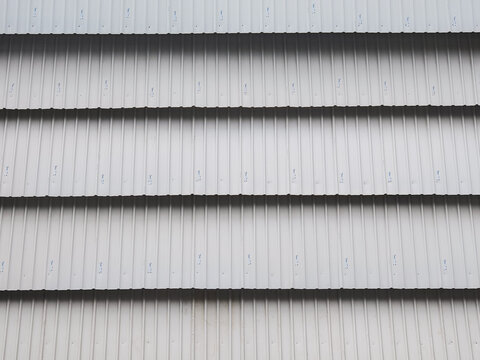 An abstract architectural background featuring horizontal rows of white corrugated metal siding panels with sharp shadows and industrial stamps
