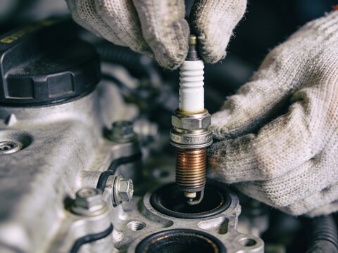 Mechanic installing a new spark plug into a car engine block in a garage