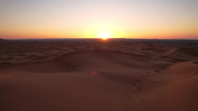 Sunrise rises above the Erg Chebbi dune sea near Merzouga, Morocco, illuminating endless Saharan formations and flowing sand textures across the desert landscape, drone forward flight shot.