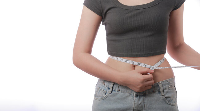 Determined young woman measures waist using tape measure during her healthy weight loss journey showing hopeful confident expression against white background