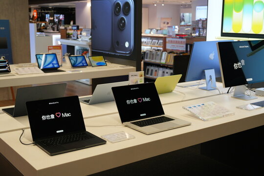Apple laptops and desktop computers displayed in an electronics store.