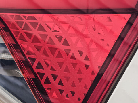An abstract close-up macro view of a modern red automotive taillight lens featuring a repeating triangular geometric mesh pattern and clean structural lines