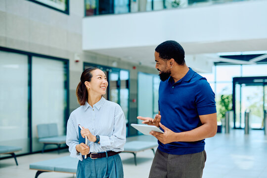 Professional coworkers discussing project, using digital tablet, smiling in a contemporary building hallway, fostering communication and teamwork