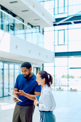 Fototapeta premium Multiracial business professionals discussing data and working together on a tablet, fostering teamwork and partnership in a corporate setting
