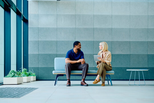 Two diverse business people having a discussion while collaborating and looking at a digital tablet in a modern office lobby