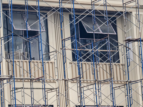 An abstract geometric close-up view of interlocking blue and silver industrial metal scaffolding pipes set against a modern concrete building exterior.