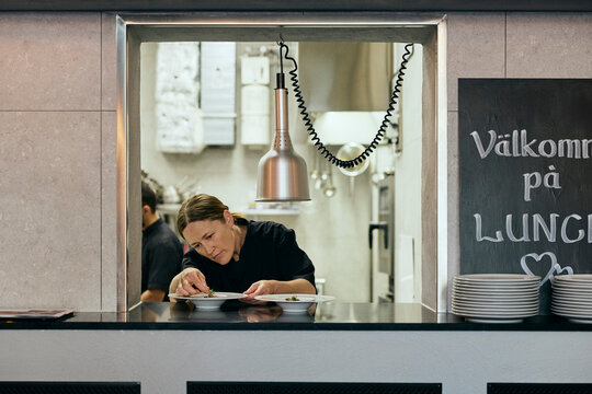 Dedicated female chef garnishing dishes at kitchen pass window
