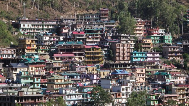 Forest trees beautifully frame a bustling Himalayan hillside settlement under clear daylight skies.