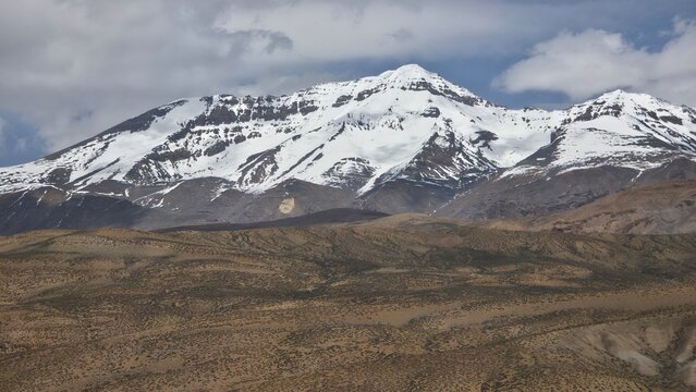 Towering snow-covered Himalayan peaks dominate the rugged landscape beneath dramatic cloud-filled mountain skies.
