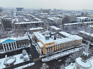 Obraz premium Aerial view focusing on large, ornate government or public buildings with prominent columns and towers, covered in a light layer of winter snow