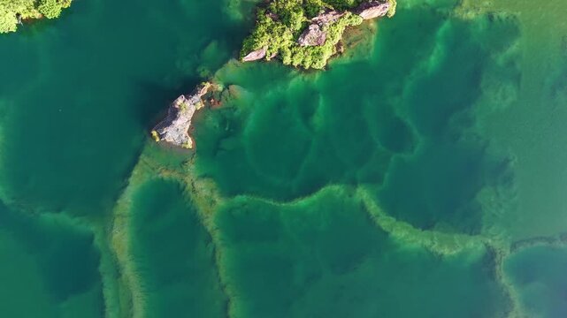 Drone footage shows an abandoned quarry lake with rocky islets and visible submerged terraces.