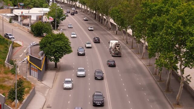 Aerial view of cars and vehicles driving along a multi-lane highway next to the mtkvari river, with the modern cityscape of tbilisi, georgia, expanding into the hillside in the background